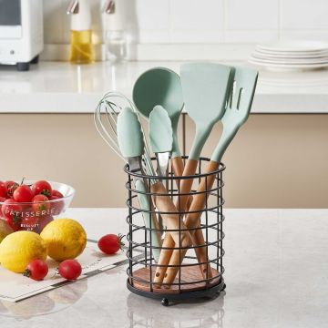 Black round cutlery holder basket with dark brown wooden base on a kitchen countertop